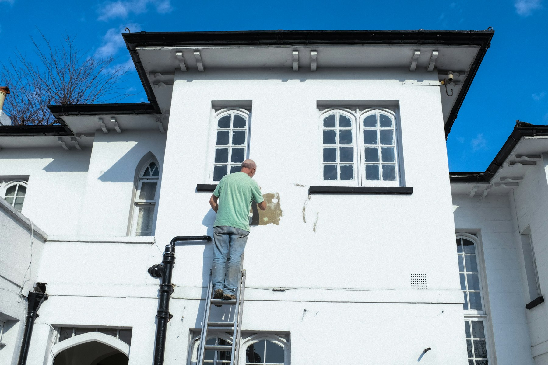 Painter on a ladder finishing a white two-story house exterior